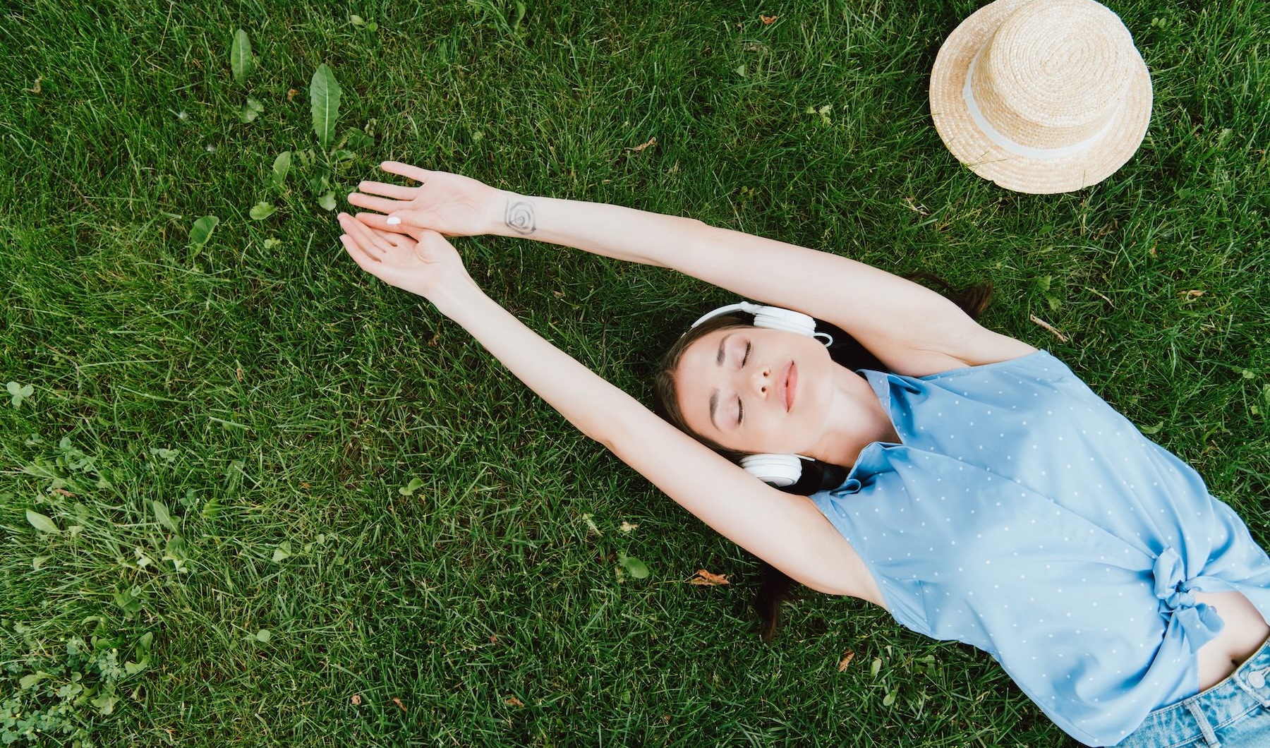 a person laying in the grass with headphones on and a hat near them