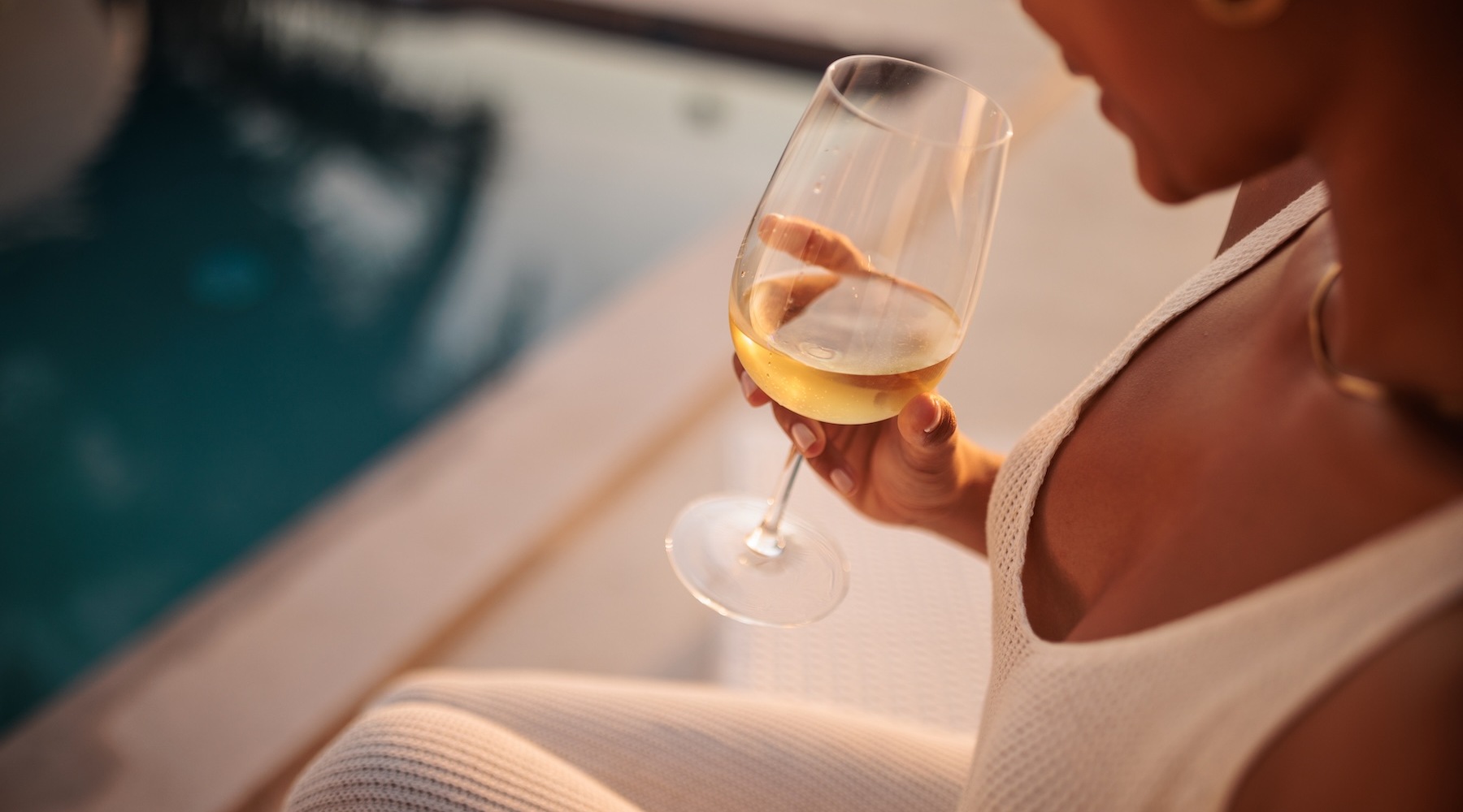 as person sitting but the pool holding a glass of wine